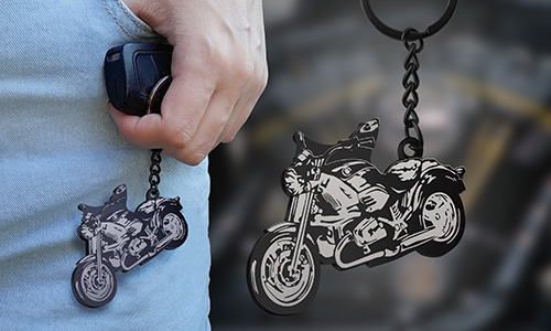 Motorcycle-shaped keychain with silver accents hanging from jeans pocket, mechanical-themed background