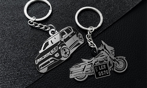 Two metallic keychains on black texture: one shaped like SUV, one shaped like motorcycle with silver details