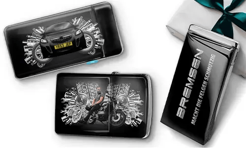 Elegante Geschenkboxen mit einem blauen Auto und einem Biker, umgeben von metallischen Zahnrädern. Eine Box trägt den Text „BREMSEN Macht Die Regeln Schmutzig“, was einen dynamischen, kantigen Ton hinzufügt.