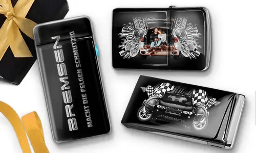 Elegante schwarze Feuerzeuge mit Auto-Designs. Eines zeigt eine Familie in einem Auto, ein anderes ein blaues Auto mit karierten Flaggen. Daneben liegt eine Geschenkbox mit goldener Schleife.