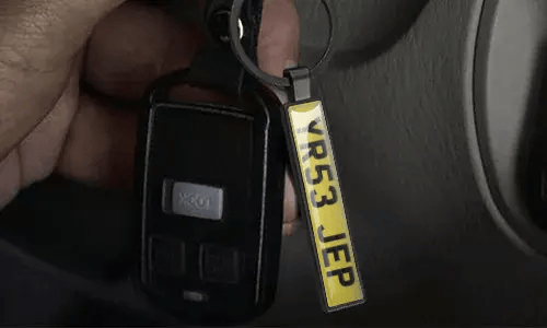 Llavero plateado de placa de matrícula cuelga de las llaves del coche dentro del vehículo