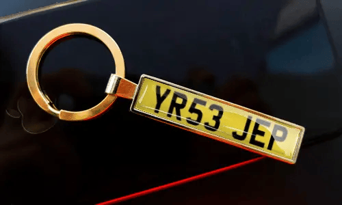 License plate keychain attached to keys in pocket with car in background