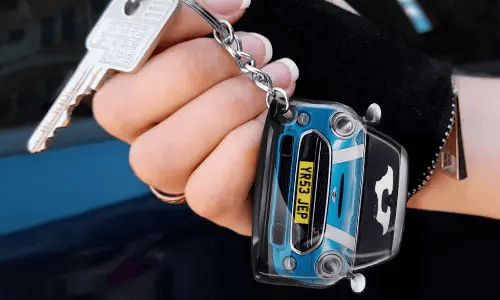 Hand hält einen Schlüsselanhänger in Form eines blauen Autos mit detaillierter Frontansicht