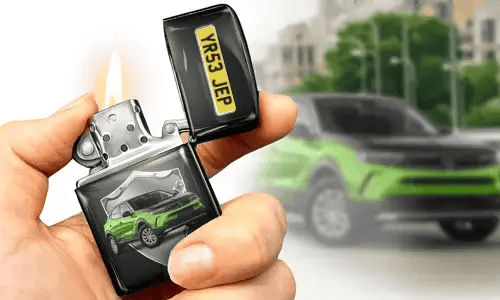 A hand holds a lit lighter with a green car image and license plate on it. A blurred green car is in the background, matching the lighter's design.
