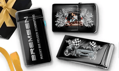 Sleek black lighters with car-themed designs. One features a family in a car; another shows a blue car with checkered flags. Gift box with gold ribbon nearby.