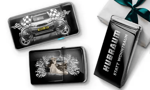 Three black wallets with car-themed designs and checkered flags, set against a white background. One shows a car with wheels, another features a couple, and one has 