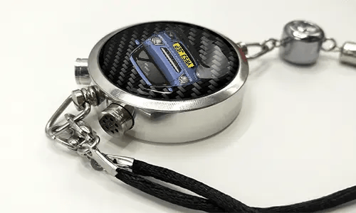 Round car key fob with carbon fiber face, buttons labeled LOCK and UNLOCK, braided black cord attached