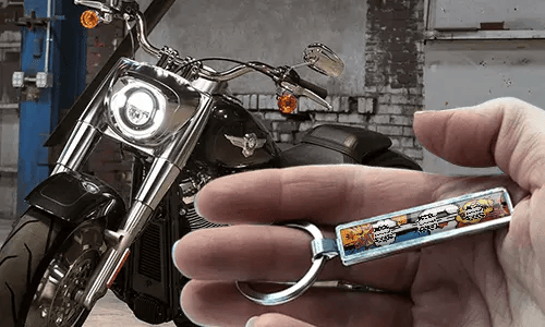 Brelok z tablicą rejestracyjną w stylu komiksowym, trzymany w dłoni, z motocyklem w tle