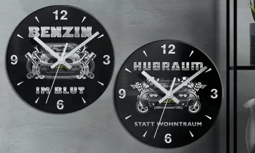 Zwei schwarze Wanduhren mit Autoillustrationen und deutschem Text: BENZIN IM BLUT und HUBRAUM STATT WOHNTRAUM