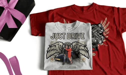 Zwei T-Shirts mit auffälligen Grafiken, eines weiß mit JUST DRIVE und Paar am Auto, eines rot mit geflügeltem Motor und Flammen, neben Geschenkbox mit rosa Schleife